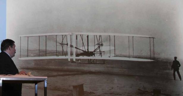 Ein Mann hält einen Vortrag vor einem Bild des Wright-Flyers.