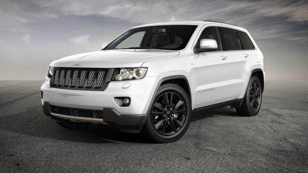 Ein weißer Jeep Grand Cherokee mit schwarzen Felgen steht auf einer asphaltierten Fläche.