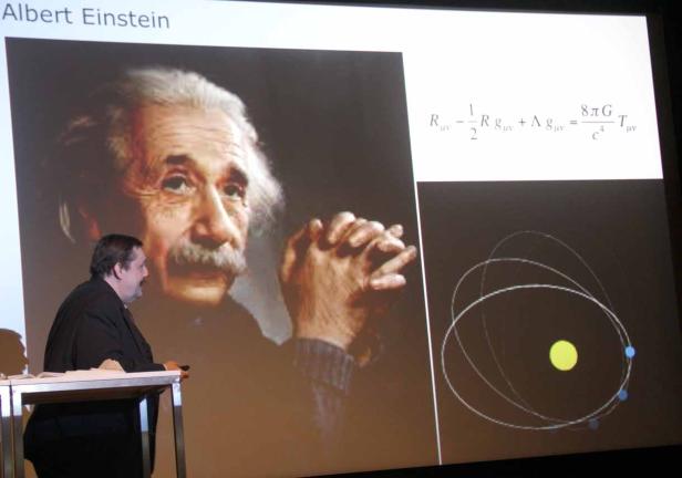 Ein Vortrag mit einem Bild von Albert Einstein und seiner berühmten Formel zur Gravitation.