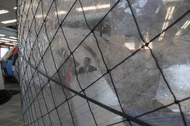 Ein Mann im Anzug steht in einer großen, transparenten Kugel, die von einem Netz umgeben ist.