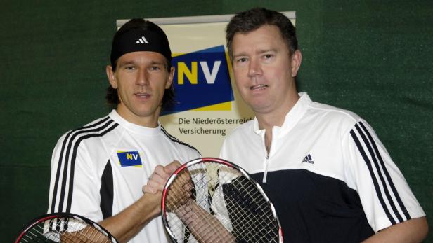 Zwei Männer im Sportdress schütteln sich die Hände vor einem Sponsorenhintergrund.