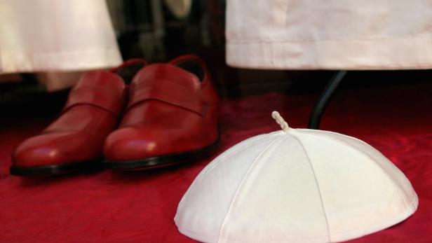 Ein Pileolus und ein Paar rote Schuhe liegen auf einem roten Tuch.