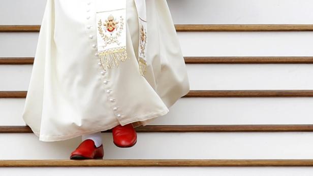 Ein Papst in rotem Schuhwerk steigt eine Treppe hinunter.