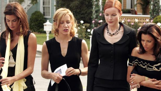 Vier Frauen in schwarzen Kleidern gehen eine Straße entlang.