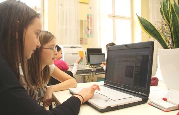 Zwei Mädchen arbeiten zusammen an einem Laptop in einem hellen Raum.