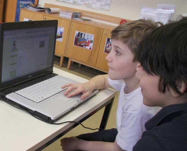 Zwei Jungen sitzen vor einem Laptop und schauen auf den Bildschirm.