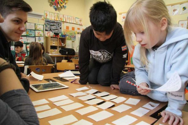 Kinder arbeiten in einem Klassenzimmer mit Kärtchen auf einem Tisch.