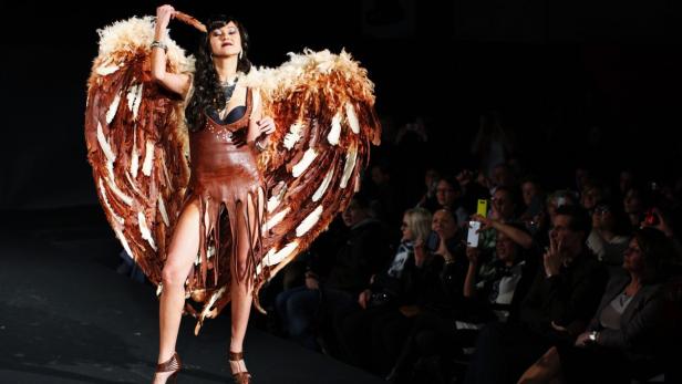 Eine Frau in einem Schokoladenkleid und Engelsflügeln posiert auf einer Modenschau.