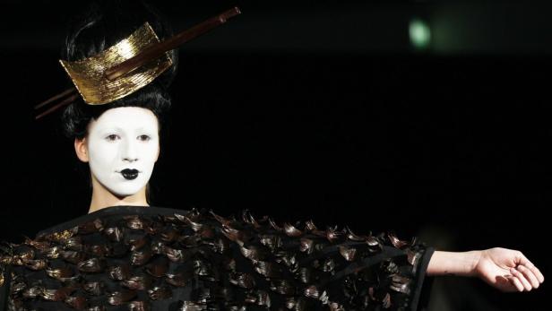 Eine Person mit weißem Gesicht und dunklem Lippenstift trägt ein extravagantes Kostüm.