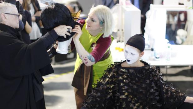 Zwei Maskenbildner arbeiten an einer Perücke und dem Make-up eines Models.