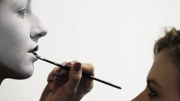 Eine Person mit weißer Gesichtsbemalung bekommt schwarzen Lippenstift aufgetragen.