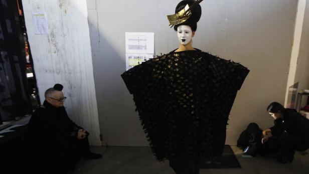 Ein Model mit weißem Gesicht und schwarzem Kleid posiert zwischen zwei Personen.