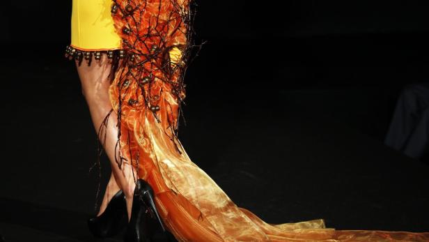 Eine Frau in einem gelben Kleid mit orangefarbenem Schleier und schwarzen High Heels.