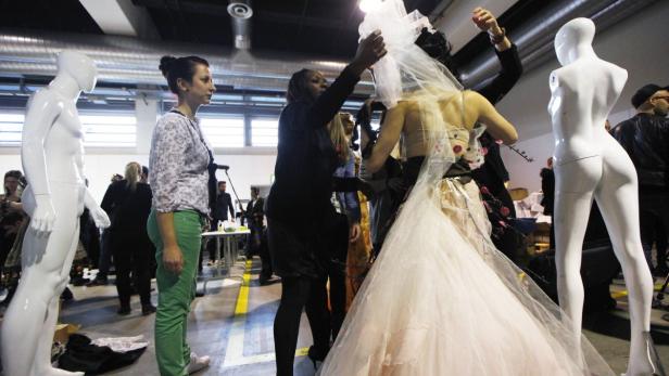 Hinter den Kulissen einer Modenschau wird ein Brautkleid mit Schleier angepasst.