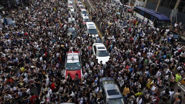 Eine große Menschenmenge blockiert eine Straße mit Autos und einem Bus.