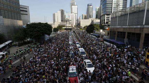 Eine große Menschenmenge blockiert eine Straße mit Autos in einer Stadt.