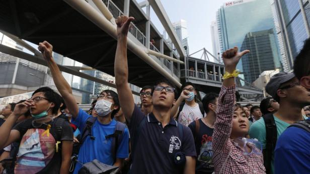 Eine Menschenmenge demonstriert mit erhobenen Fäusten in einer städtischen Umgebung.