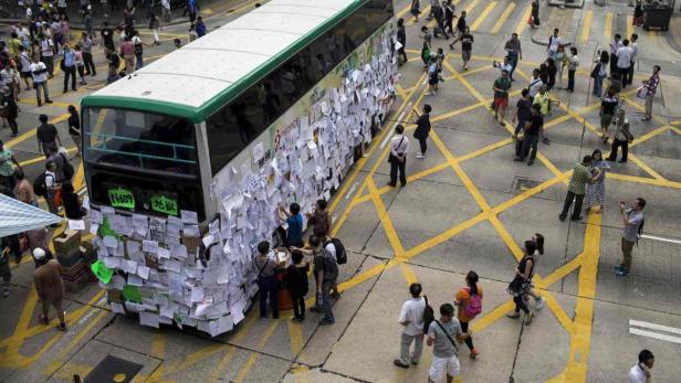 Ein Bus ist mit Zetteln beklebt, umgeben von Menschen auf einer Straße mit gelben Markierungen.