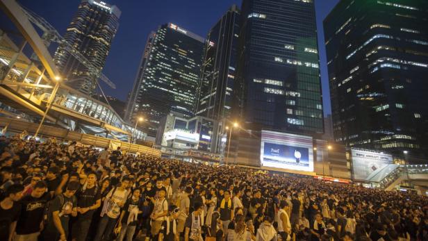 Eine große Menschenmenge versammelt sich nachts in einer Stadt mit Hochhäusern.