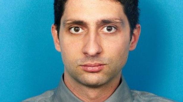 Porträt eines Mannes mit braunen Augen vor einem blauen Hintergrund.