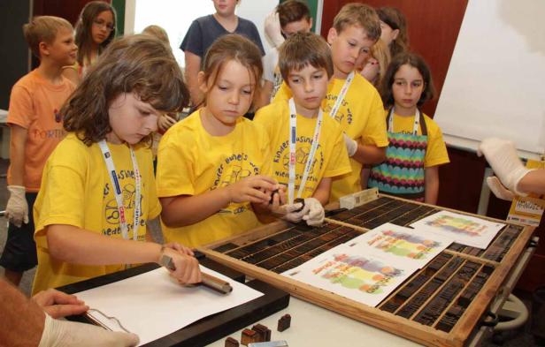 Eine Gruppe Kinder bedruckt Papier mit alten Drucktechniken.