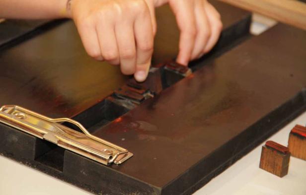 Eine Person setzt hölzerne Druckbuchstaben in eine Setzmaschine.