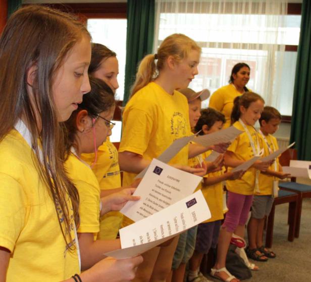 Eine Gruppe Kinder in gelben T-Shirts liest gemeinsam aus Papierbögen.