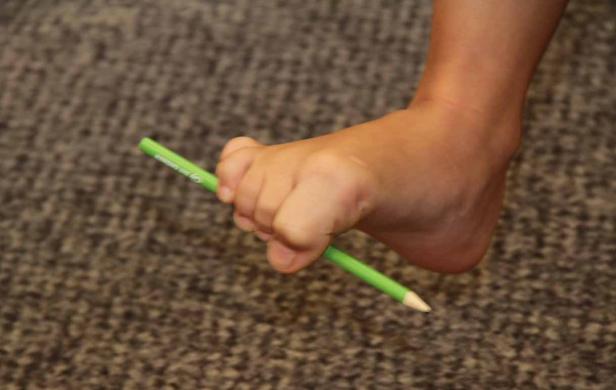 Ein Fuß hält einen grünen Stift zwischen den Zehen.