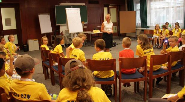 Eine Frau hält einen Vortrag vor einer Gruppe von Kindern in gelben T-Shirts.