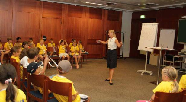 Eine Frau hält einen Vortrag vor einer Gruppe von Kindern in gelben T-Shirts.