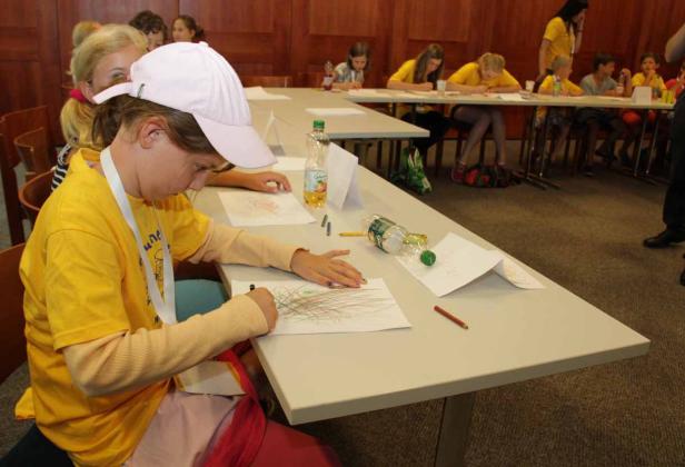 Kinder sitzen an Tischen und zeichnen mit Buntstiften auf Papier.