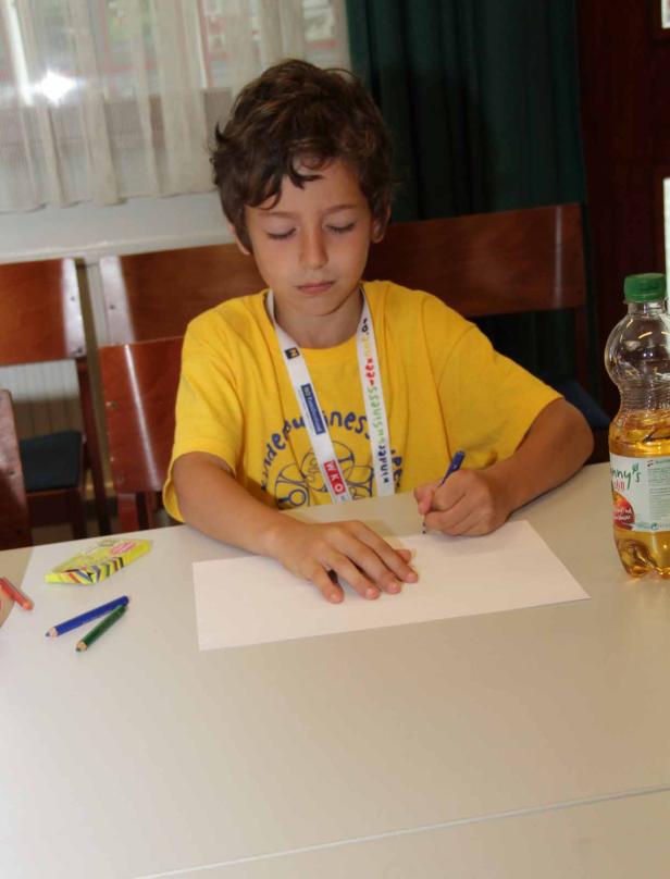 Ein Junge mit gelbem T-Shirt zeichnet auf ein Blatt Papier.