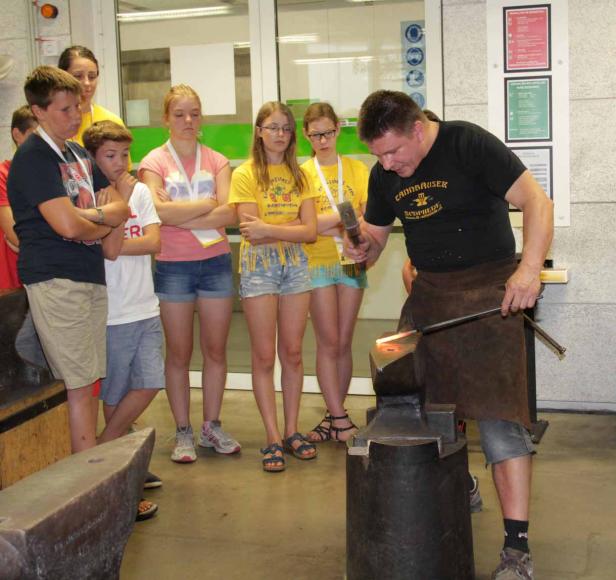 Ein Schmied demonstriert seine Arbeit vor einer Gruppe von Jugendlichen.