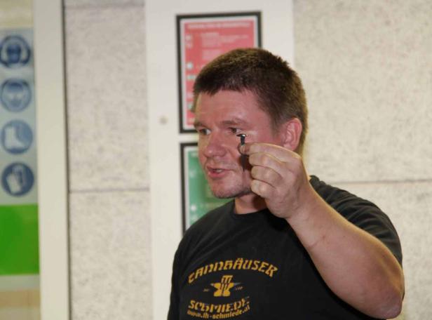 Ein Mann hält einen Nagel vor sein Auge.