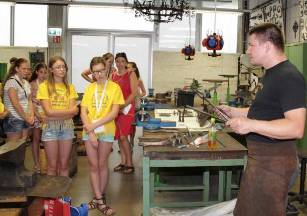 Eine Gruppe von Schülerinnen beobachtet einen Schmied bei der Arbeit in einer Werkstatt.