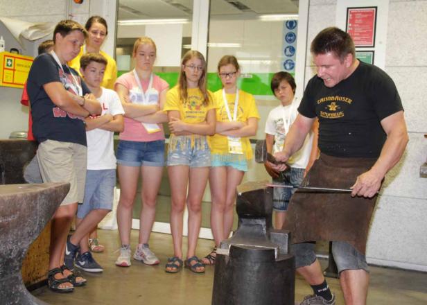 Ein Schmied demonstriert sein Handwerk vor einer Gruppe von Kindern.