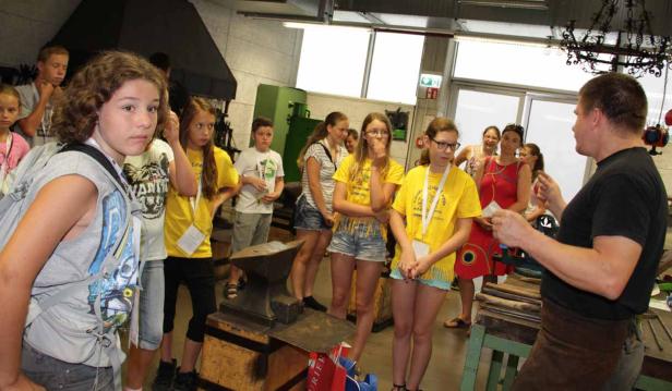 Eine Gruppe von Kindern und Erwachsenen beobachtet einen Schmied bei der Arbeit.