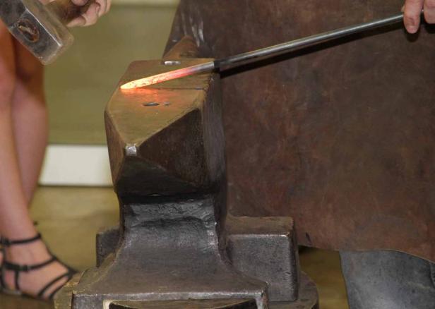 Ein glühendes Metallstück wird auf einem Amboss mit einem Hammer bearbeitet.