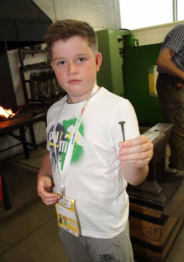 Ein Junge hält einen Nagel vor einem Amboss in die Kamera.