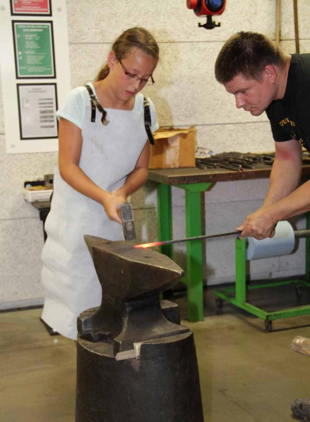 Ein Mädchen und ein Mann schmieden glühendes Metall auf einem Amboss.
