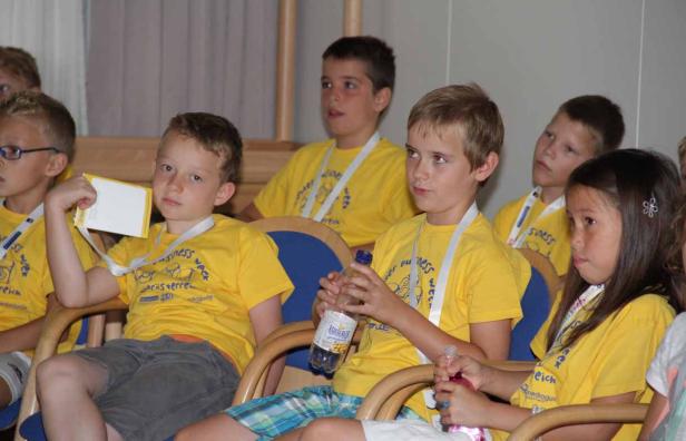 Eine Gruppe Kinder sitzt auf Stühlen und trägt gelbe T-Shirts.