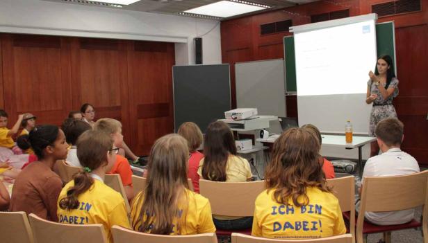 Eine Frau hält eine Präsentation vor einer Gruppe von Kindern in einem Klassenzimmer.