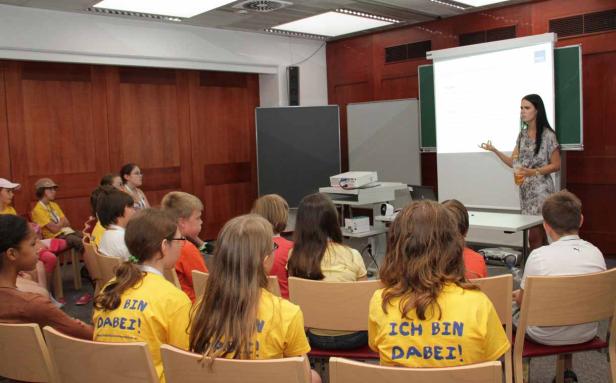 Eine Frau hält eine Präsentation vor einer Gruppe von Kindern in gelben T-Shirts.