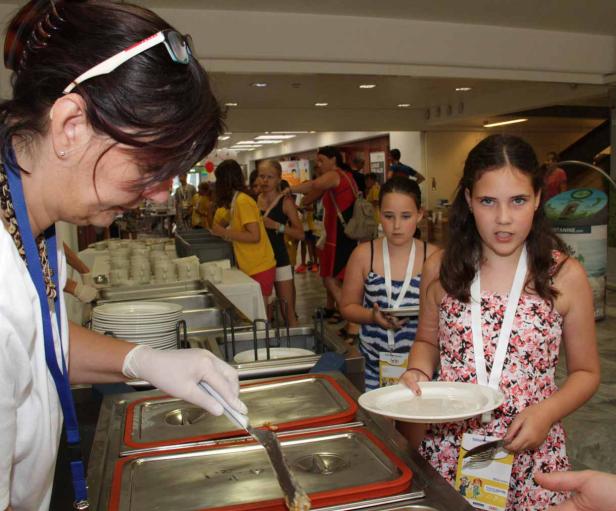 Zwei Mädchen stehen an einem Buffet und lassen sich Essen auf ihre Teller geben.