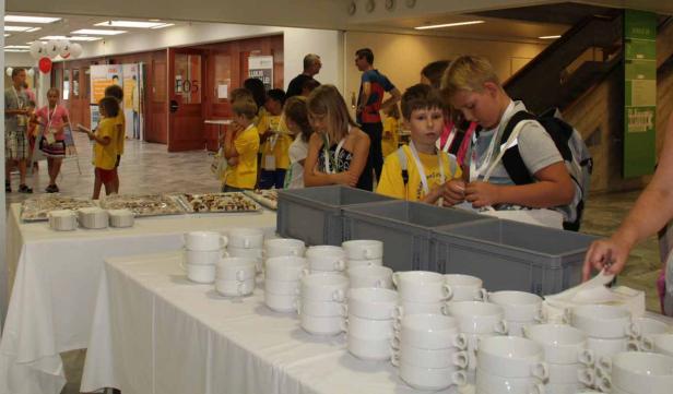 Eine Gruppe Kinder steht an einem Tisch mit Geschirr und Essen.