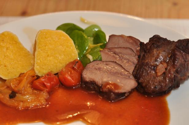 Ein Teller mit Polenta, Fleisch, Tomaten und Salat in einer roten Sauce.