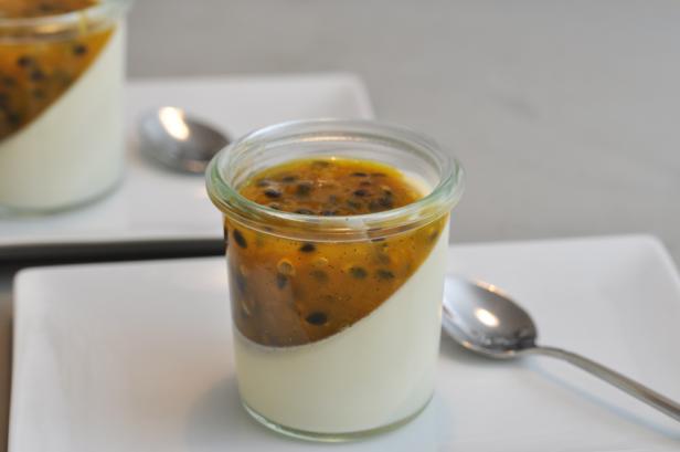 Zwei Gläser Panna Cotta mit Passionsfruchttopping stehen auf weißen Tellern.