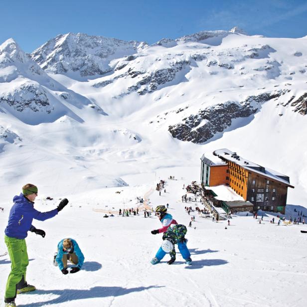 Eine Gruppe von Menschen spielt im Schnee vor einer Berghütte in den Alpen.
