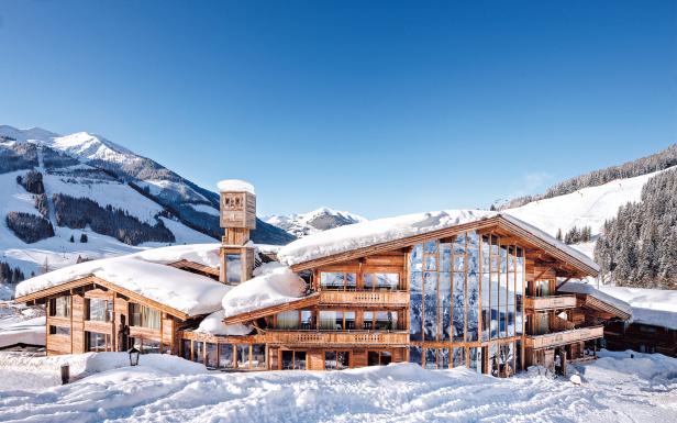 Ein luxuriöses Holzchalet im Schnee vor einer verschneiten Berglandschaft.