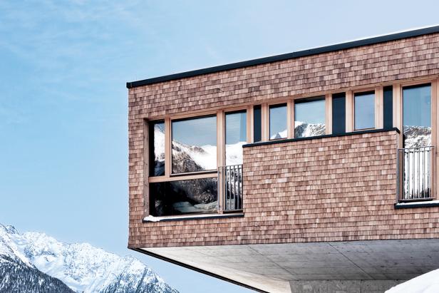 Ein modernes, mit Holzschindeln verkleidetes Gebäude vor einer verschneiten Bergkulisse.